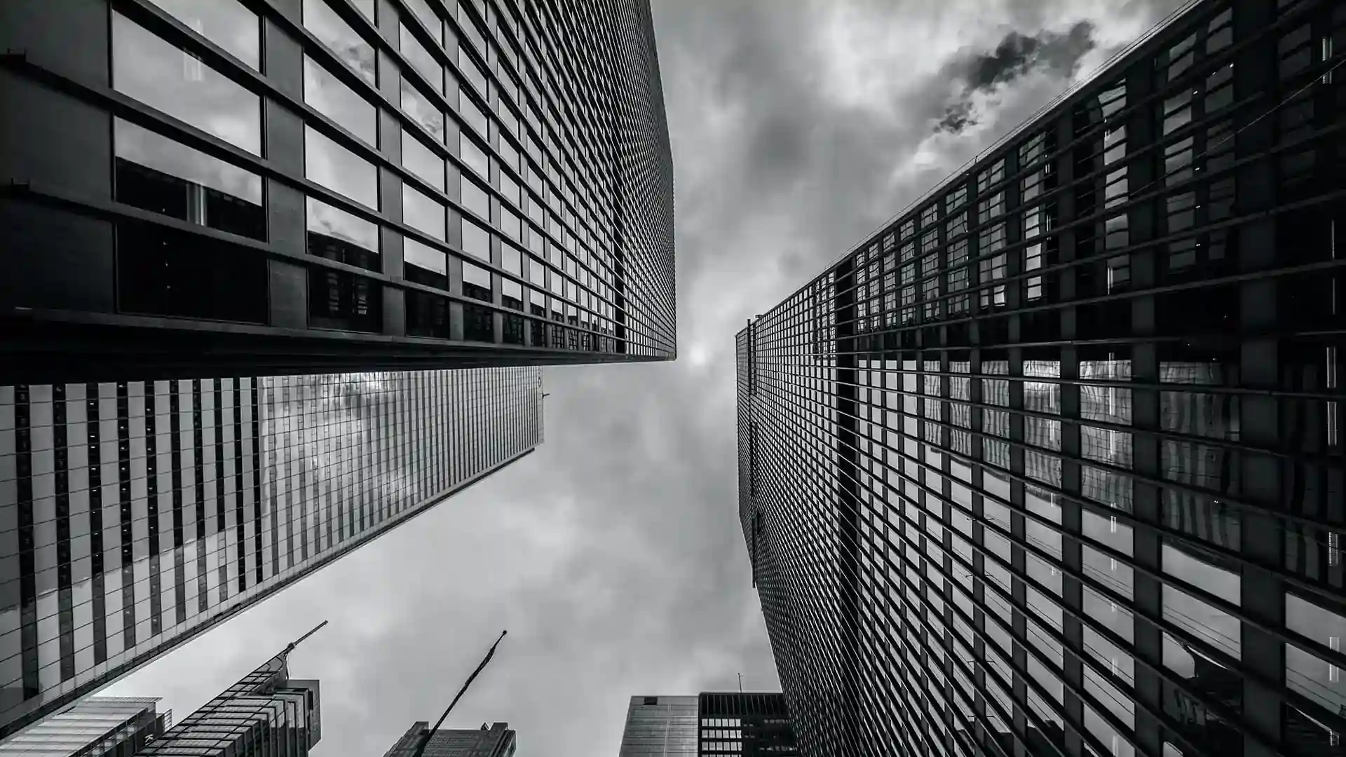 Dramatic B&W photo: Sky-high view of sleek, reflective skyscrapers against a dark, cloudy sky.